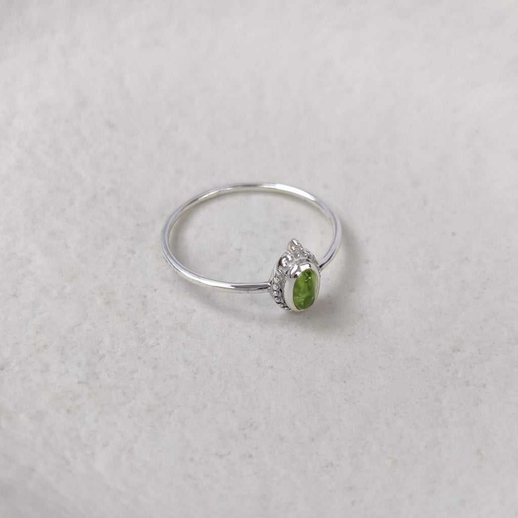 Silver ring with a green gemstone on a white surface.