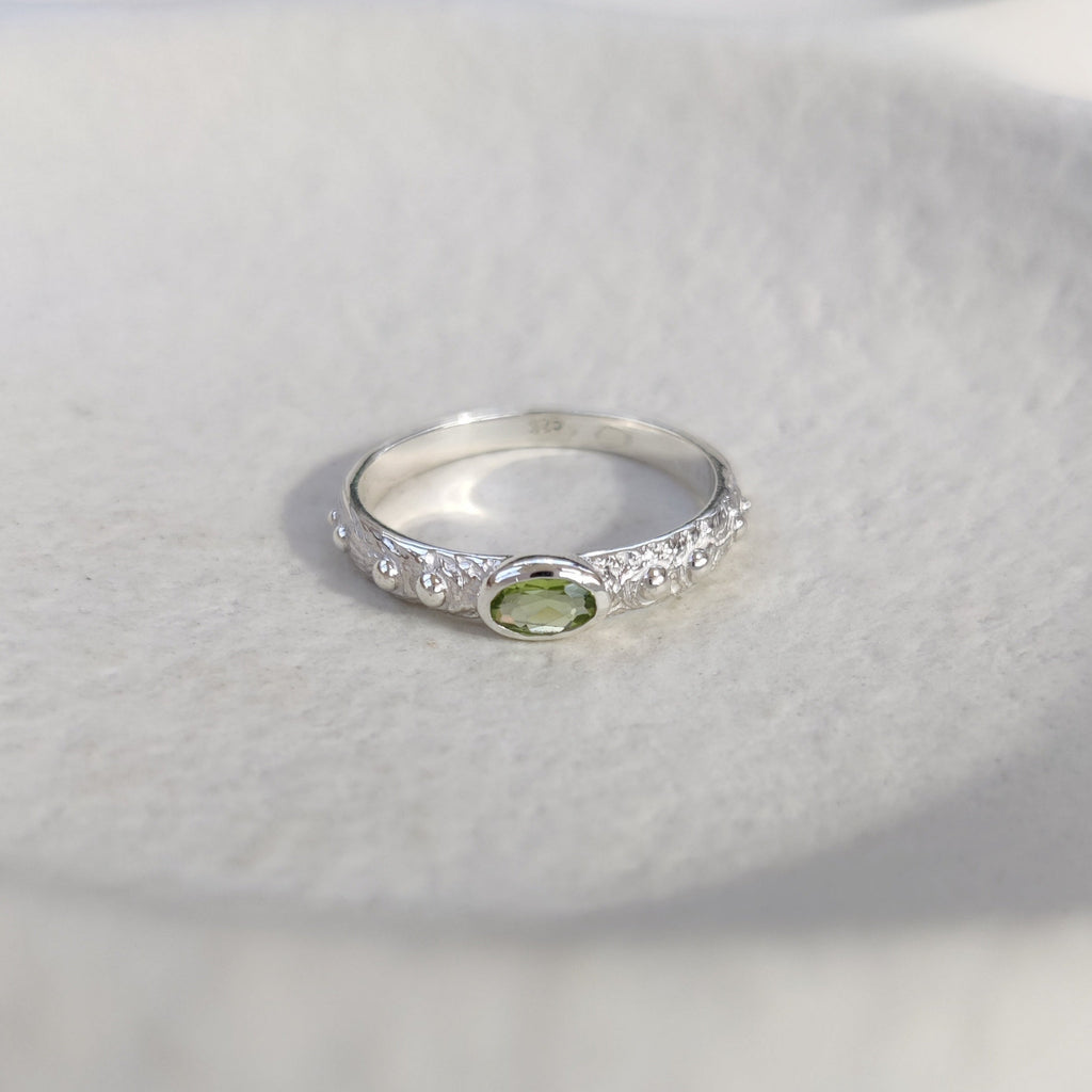 Textured silver ring with a green gemstone on a white surface. Front angle.