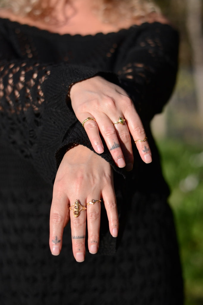 Close-up of hands with multiple gold rings with peridot and tattoos, wearing a black textured garment.