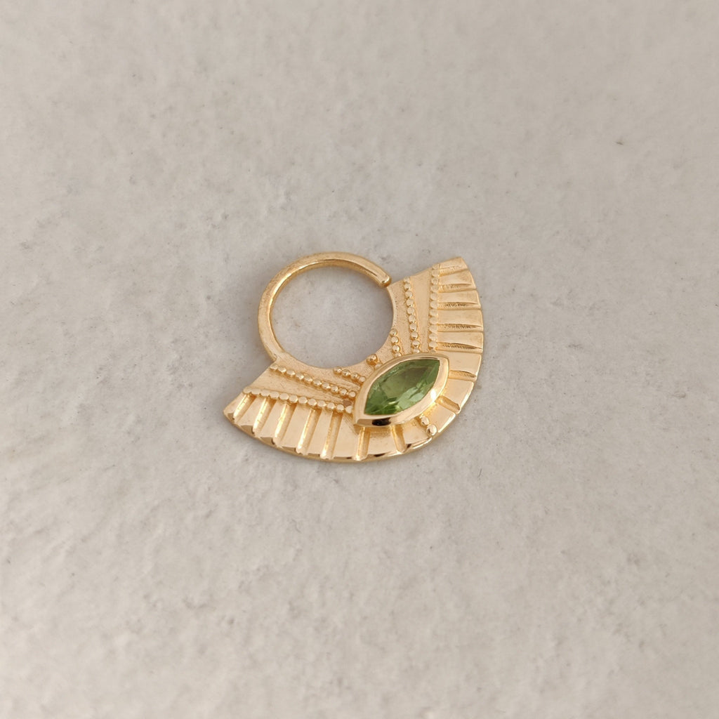 Gold septum nose ring with a green gemstone on a light background.