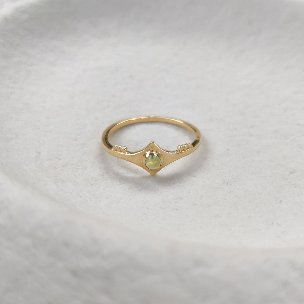 Gold ring with a green gemstone on a textured white surface.