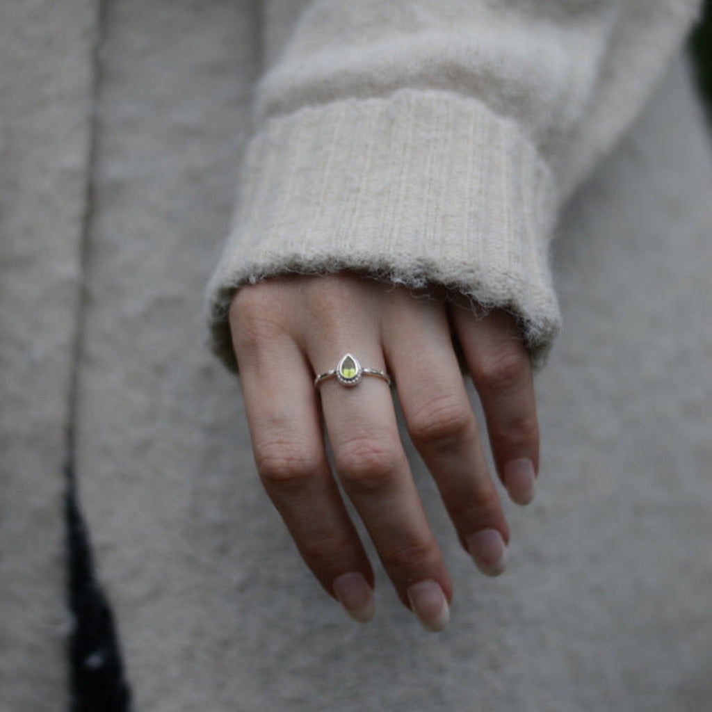 Close-up of a person's hands wearing green gemstone silver rings with a neutral background.