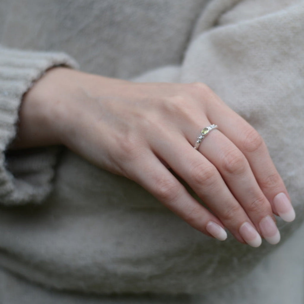 Hand wearing a textured silver ring with a green gemstone with a blurred background.