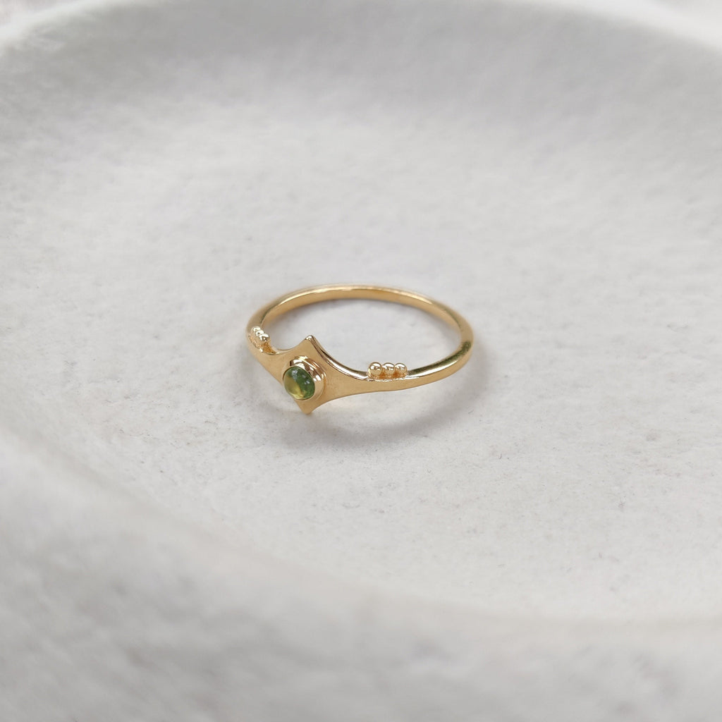 Gold ring with a green gemstone on a textured white surface.