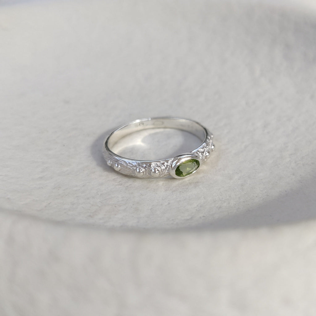Textured silver ring with a green gemstone on a white surface.