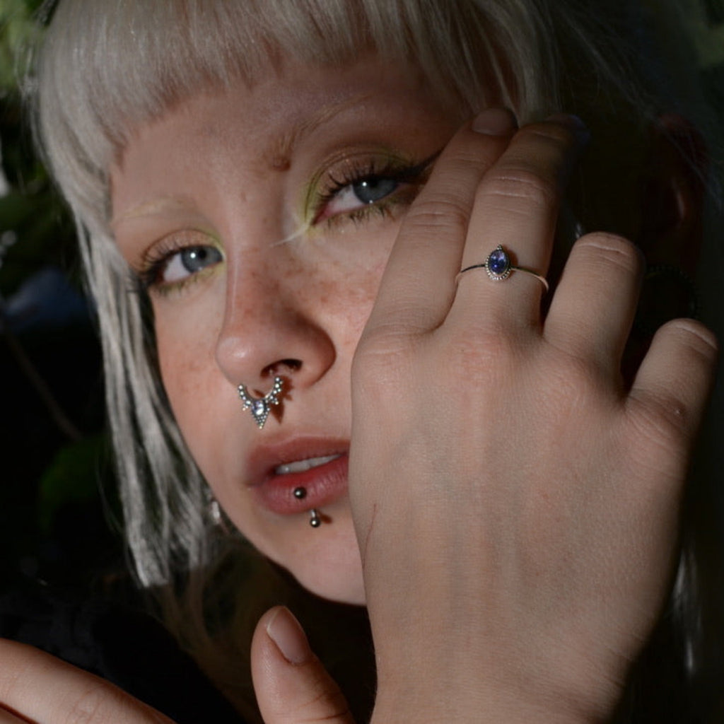 Person with multiple piercings holding her hand near her face against a dark background