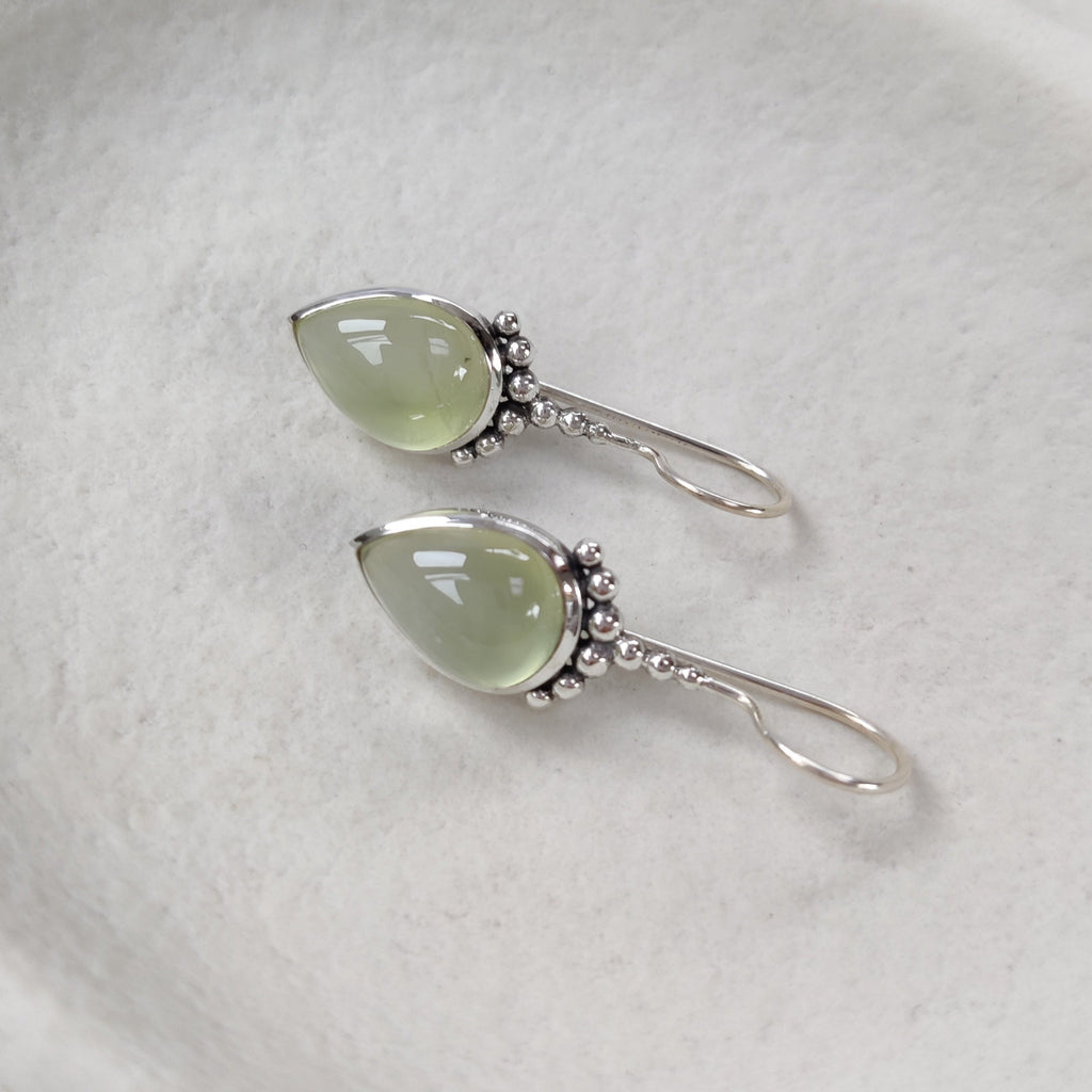 Pair of earrings with green gemstones on a white ceramic dish