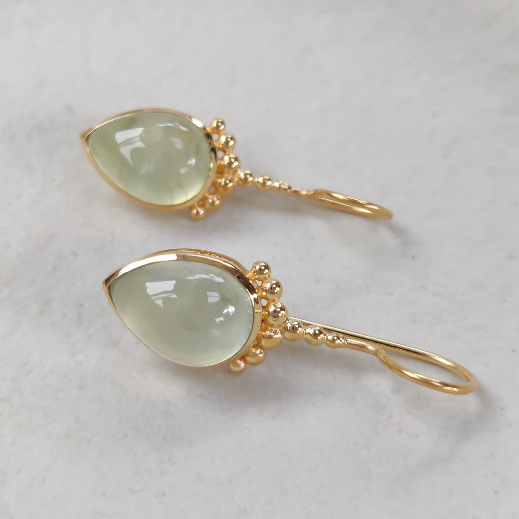 Gold earrings with green teardrop stones on a white textured surface