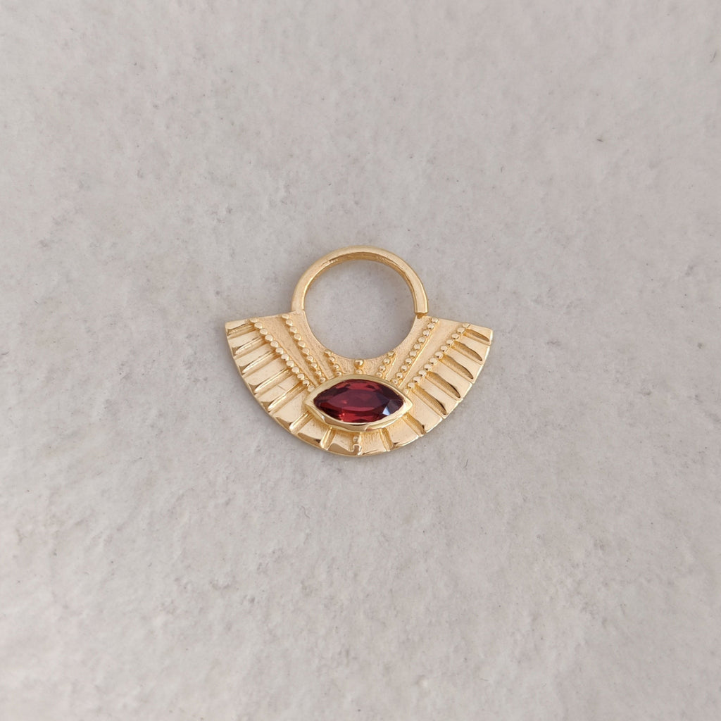 Gold septum nose ring with a red gemstone on a light background.