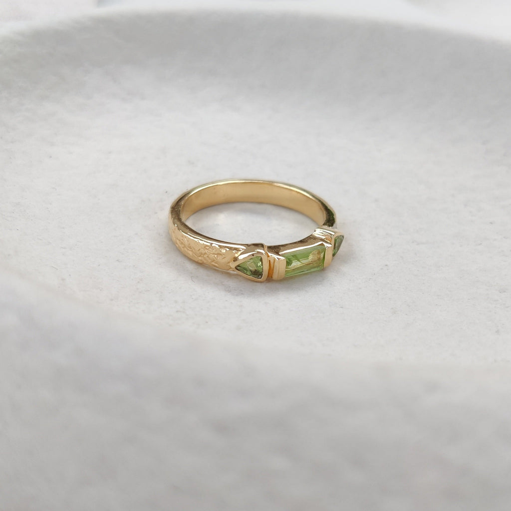 Gold ring with a green gemstone on a white background.