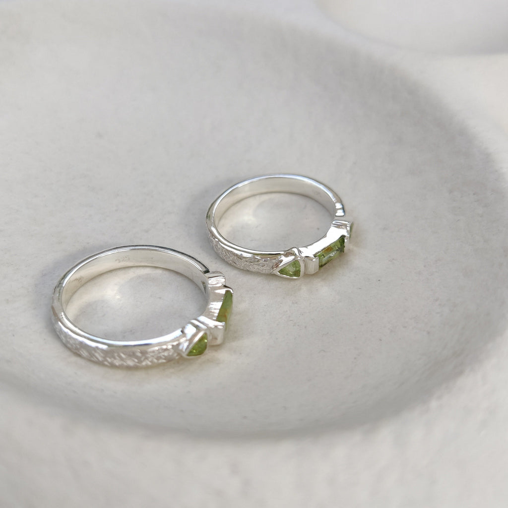 Two silver rings with green gemstones on a white surface. Displayed from two angles.