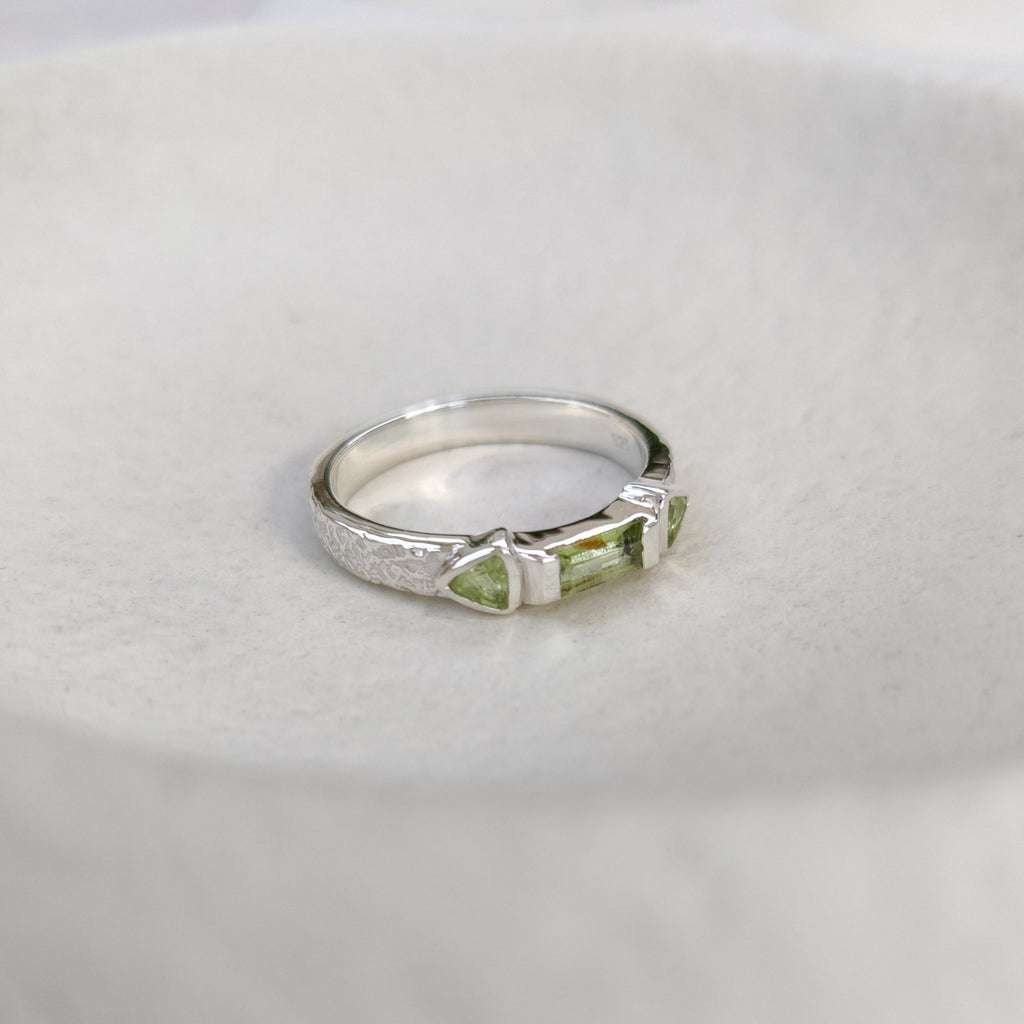 Silver ring with green gemstone on a white surface.