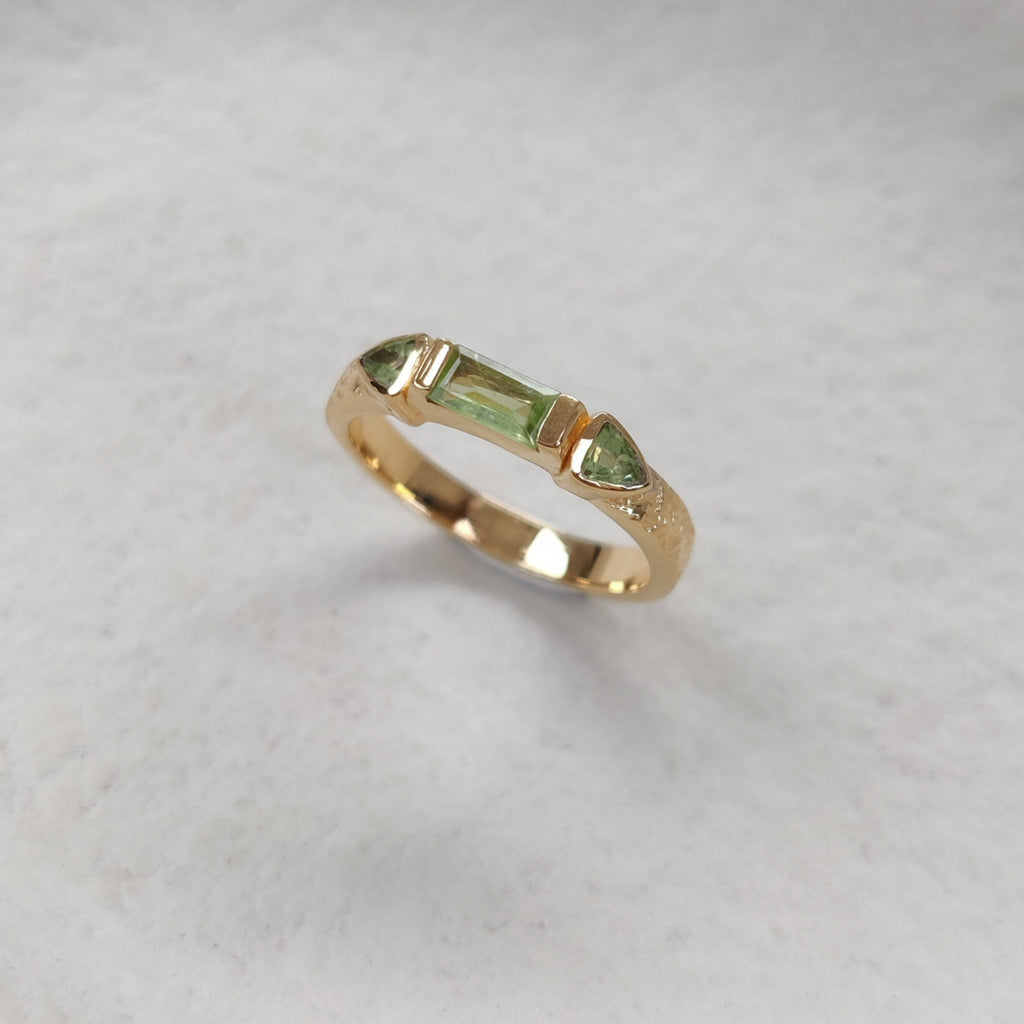 Gold ring with three green gemstones on a white background