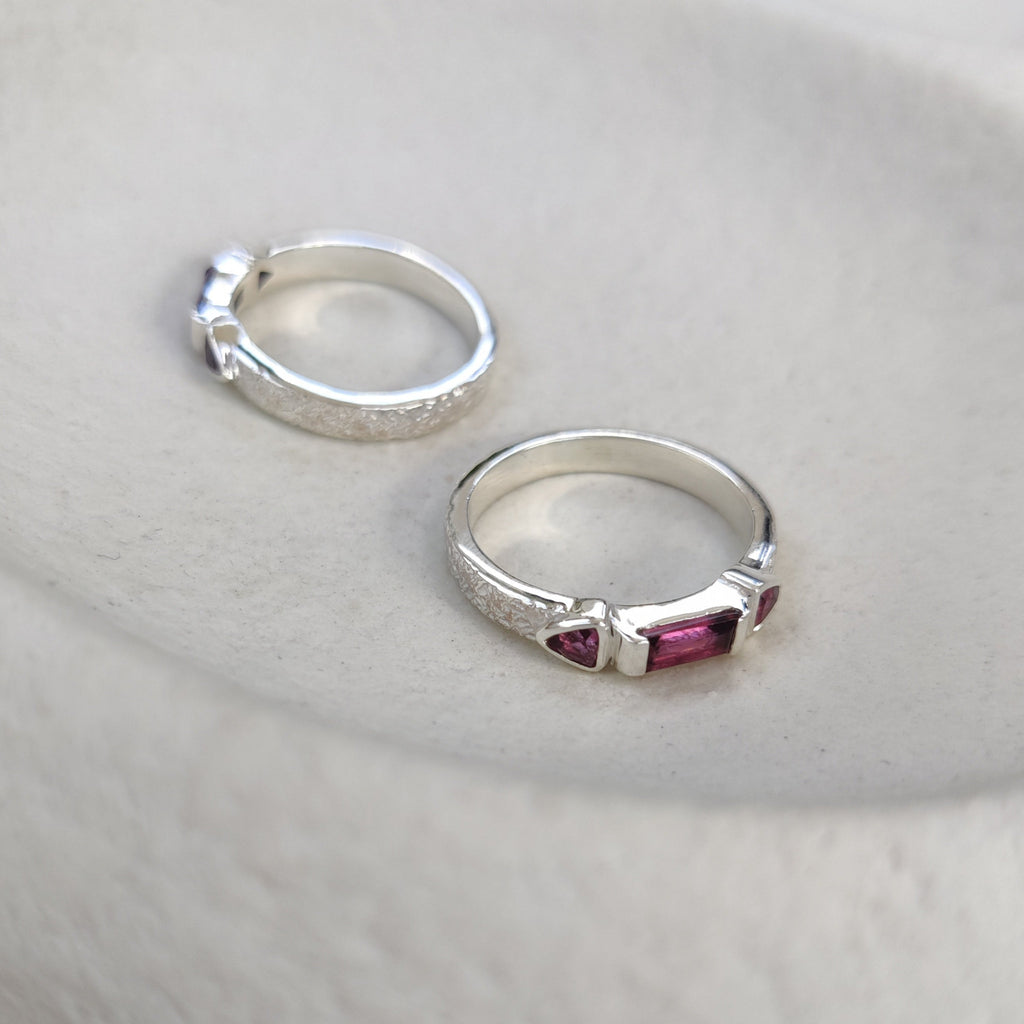 Silver ring with a pink gemstone on a textured surface.