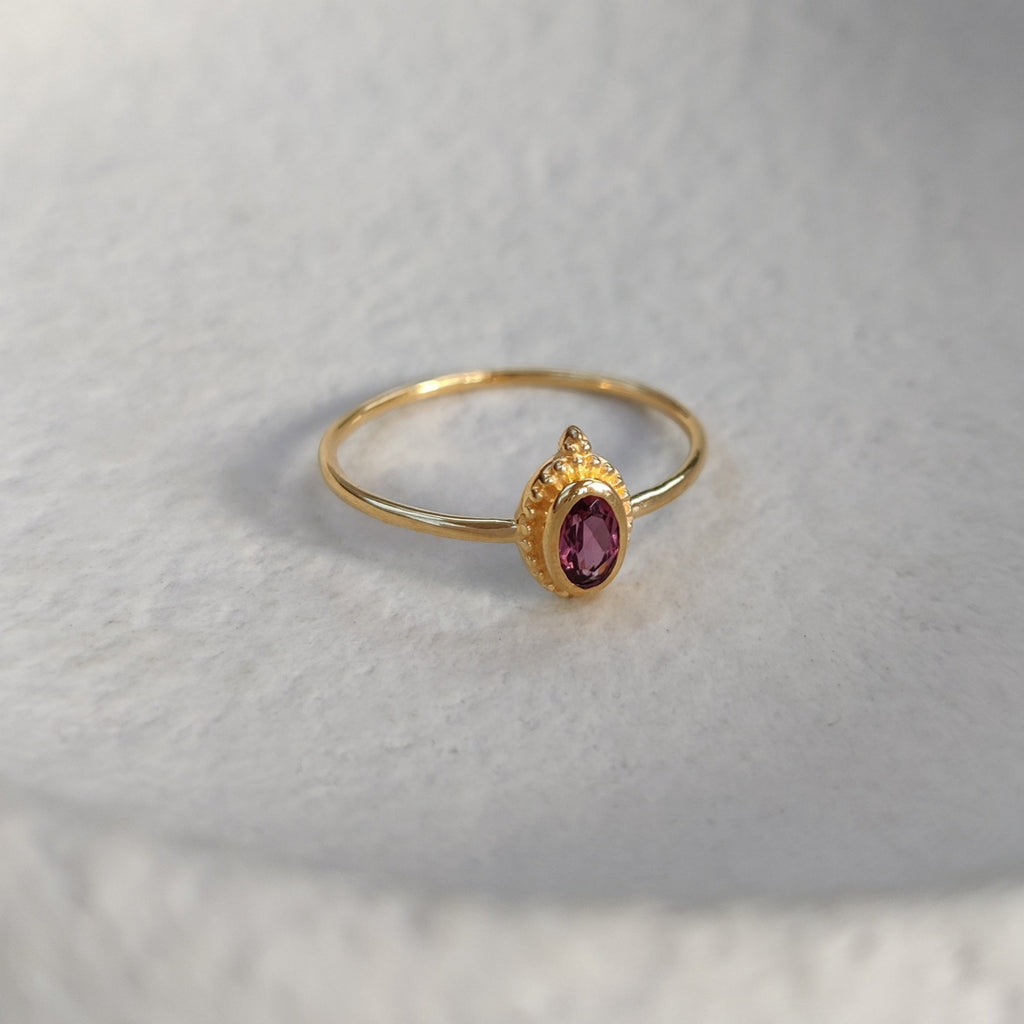 Gold ring with a pink gemstone on a textured white surface