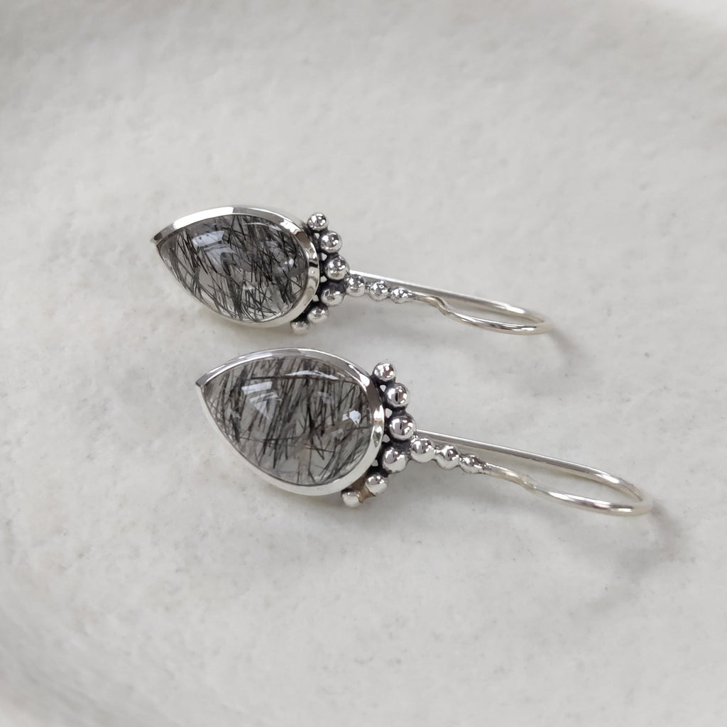 Drop-shaped silver hook earrings with rutile quartz on a white dish