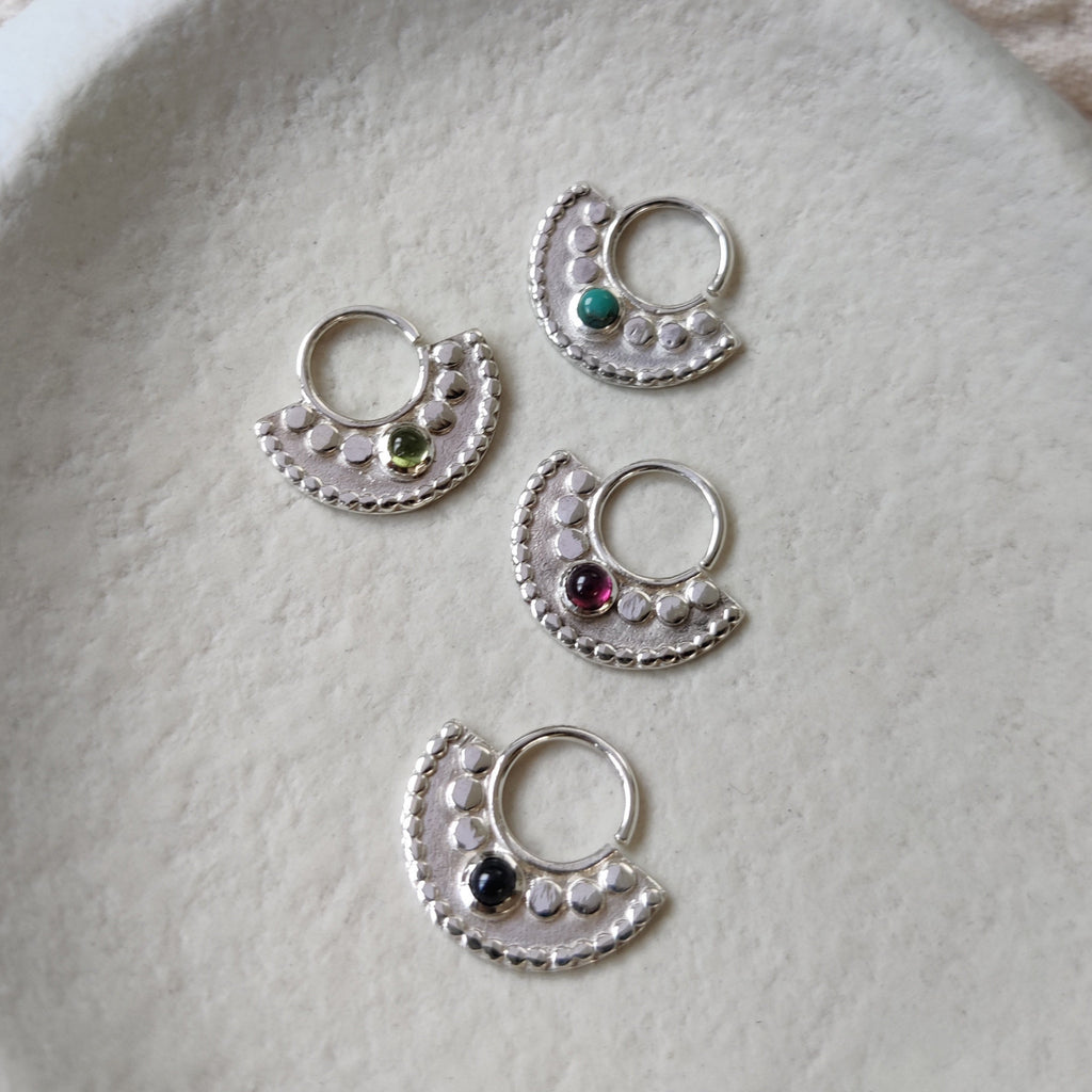 Large silver septum nose rings displayed side by side, showing the different gemstone options: turquoise, peridot, garnet and black onyx.
