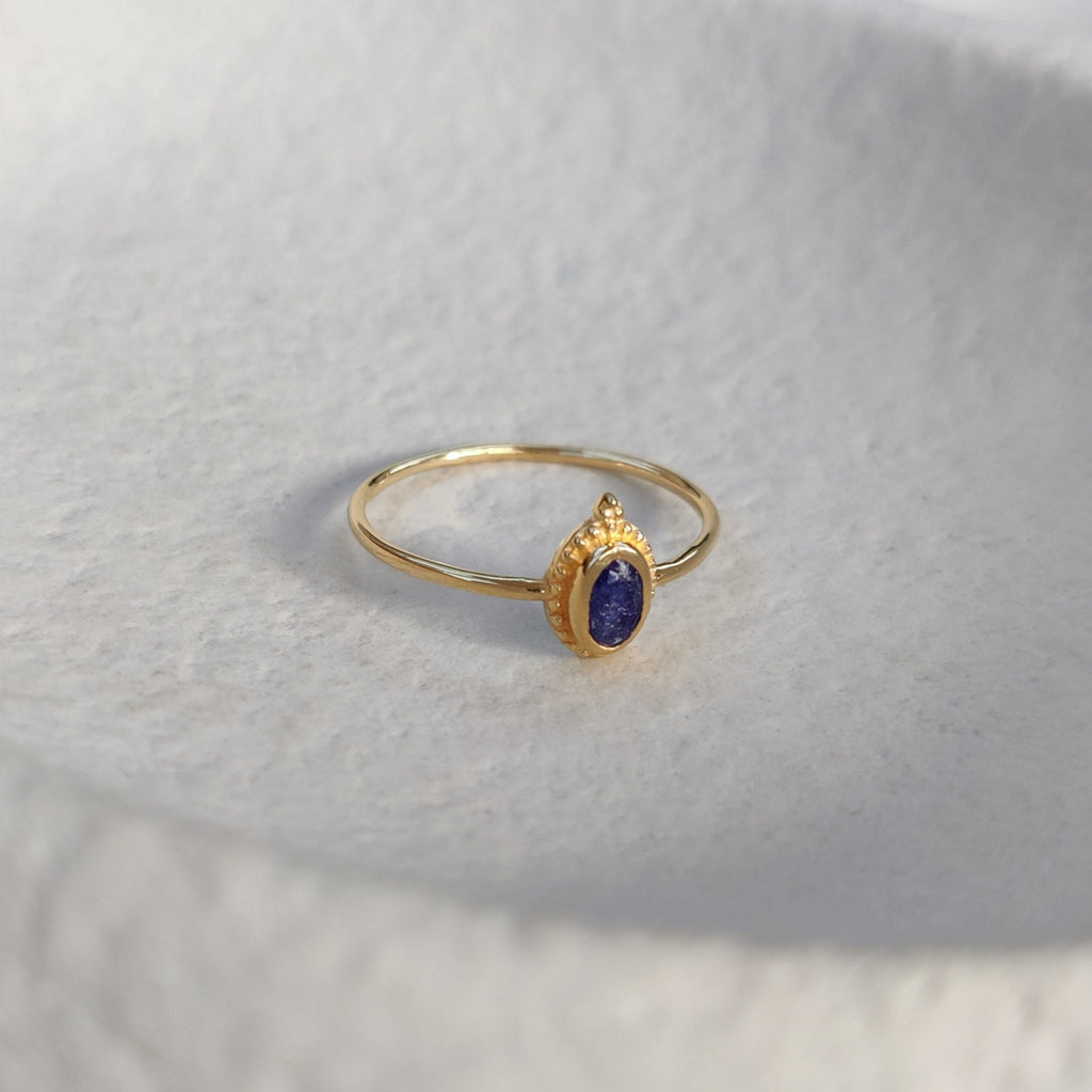 Gold ring with a blue gemstone on a textured white surface