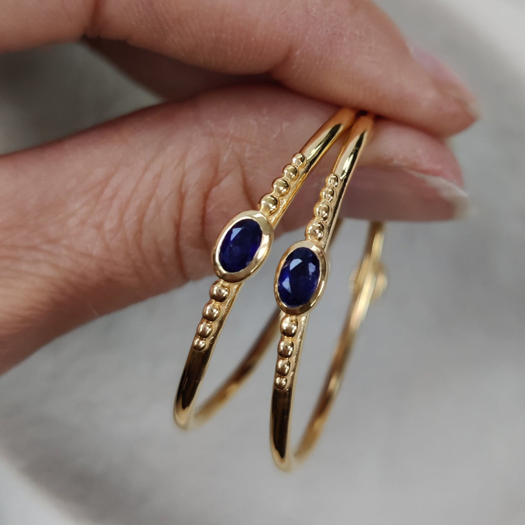 Gold rings with dark blue stones held by a hand against a neutral background