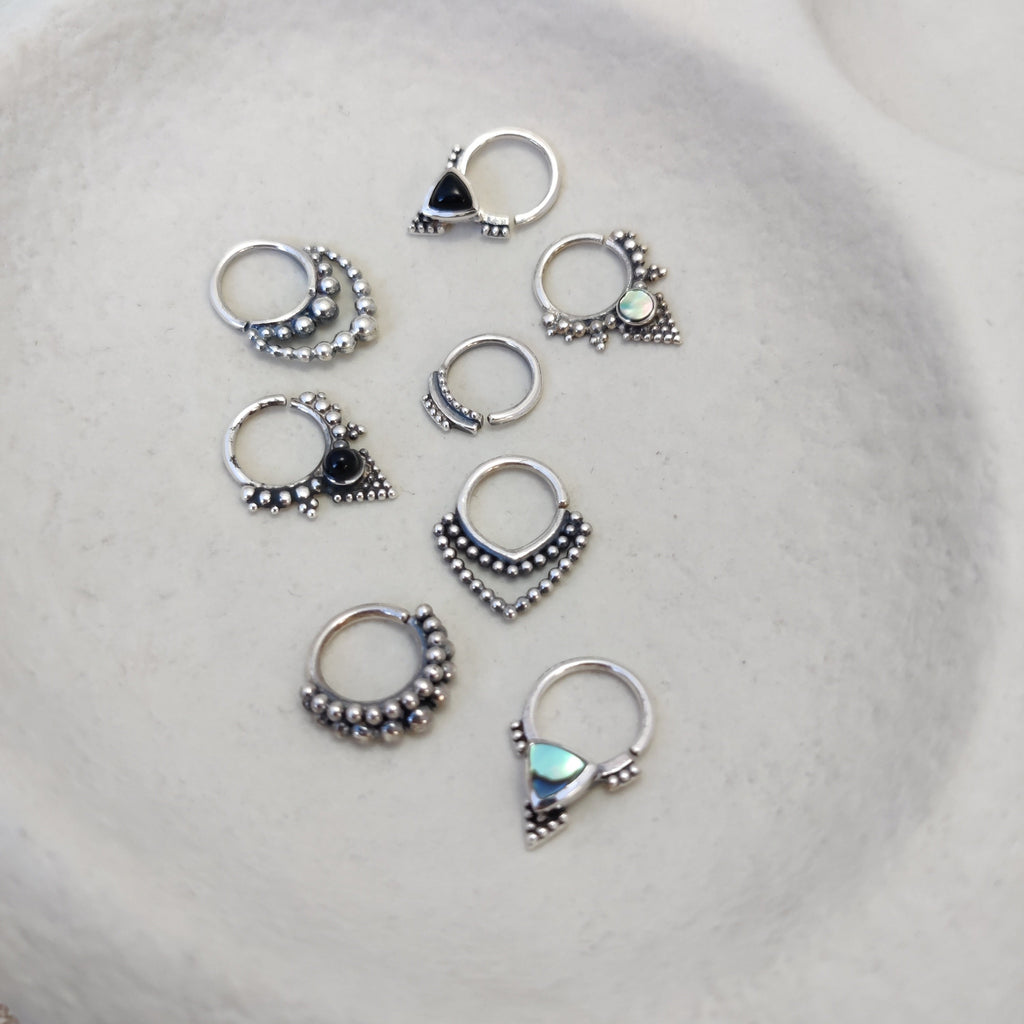 A collection of silver septum jewelry featuring intricate dotted details and gemstones, displayed to showcase their unique designs.