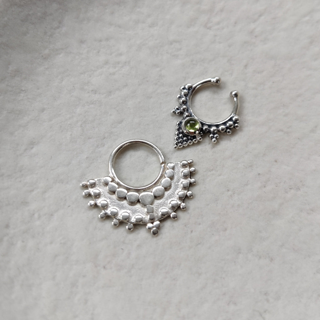 A large fan septum and a fake septum nose ring with green gemstone, displayed side by side.