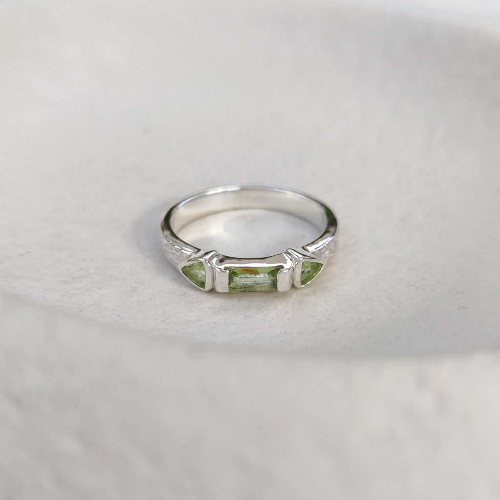 Silver ring with green gemstones on a white surface.