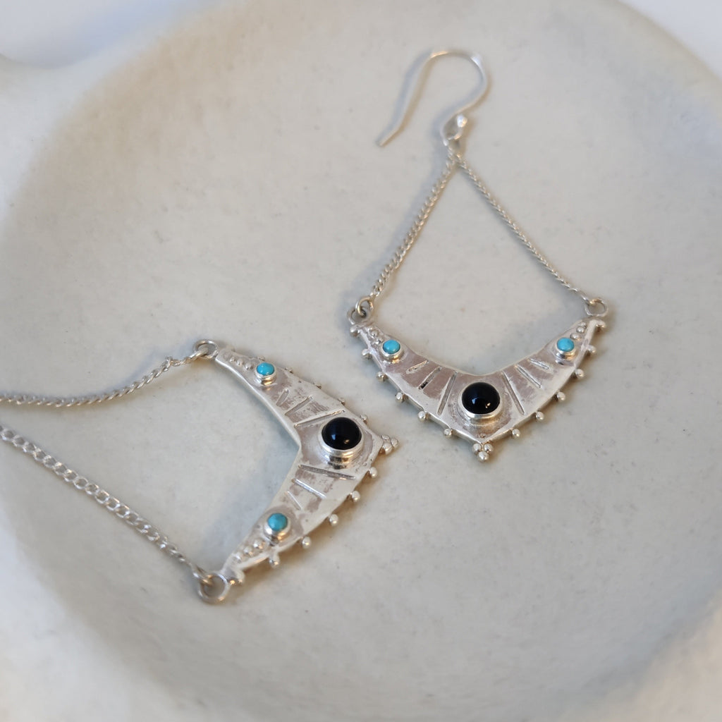 Dangling silver earrings with black onyx and turquoise, displayed on a jewelry plate.