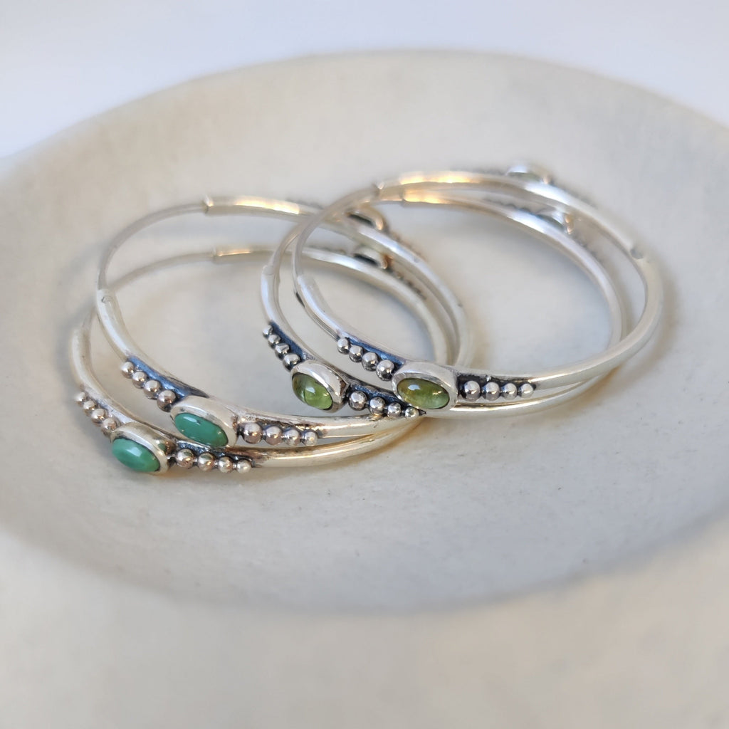 Two pairs of unique silver hoop earrings featuring dotted details and gemstones, showcasing vibrant turquoise and peridot.