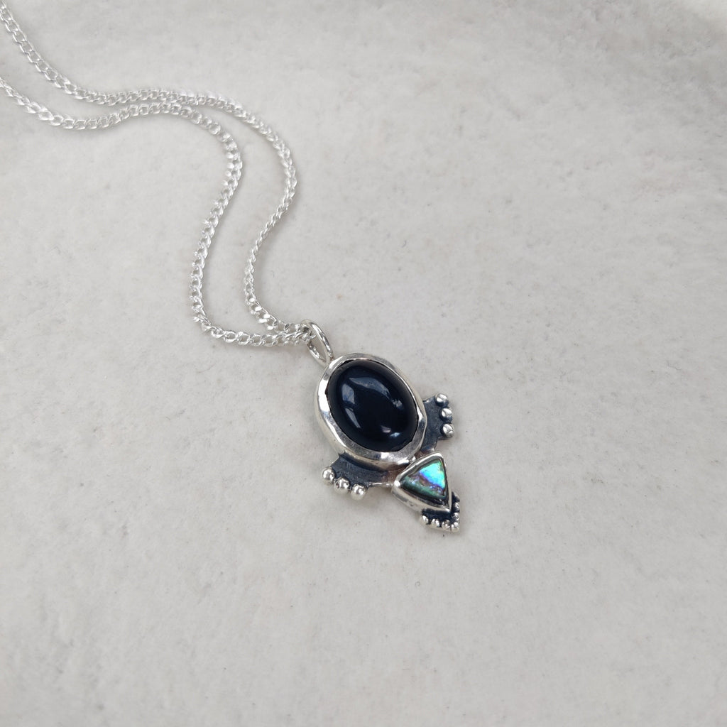 Silver necklace with a black onyx pendant on a white textured background.