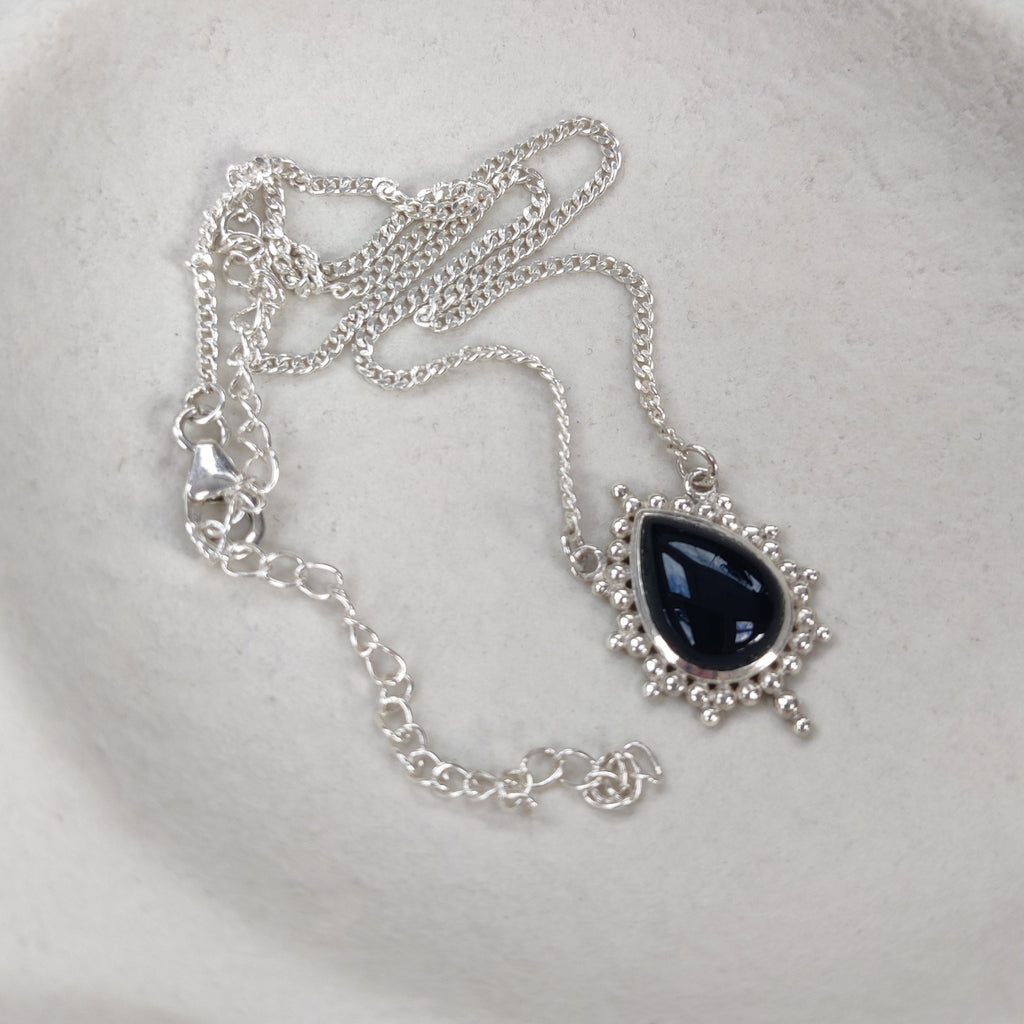 Silver necklace with a black teardrop pendant on a white surface