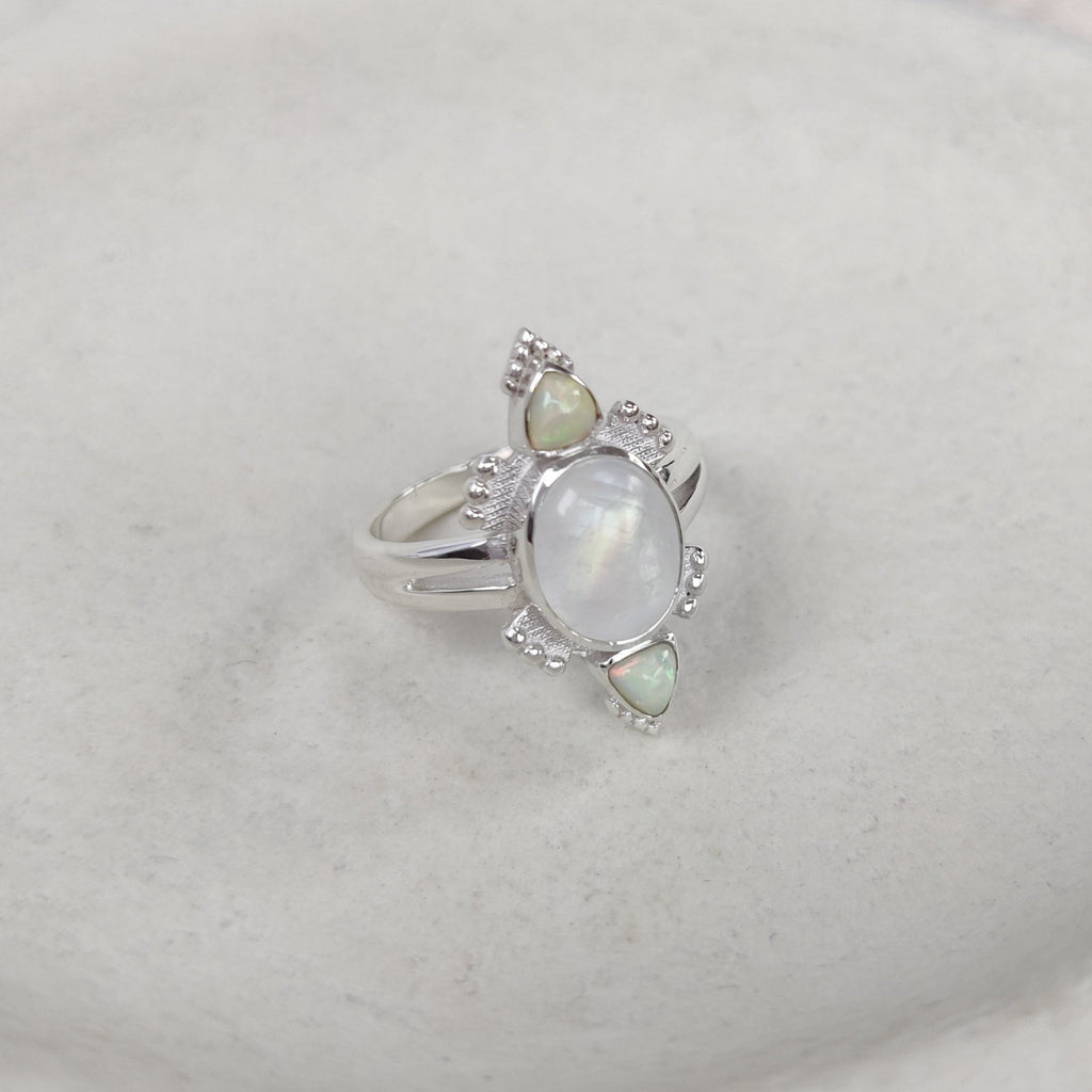 Silver ring with a oval moonstone and triangle-shaped opals on a white surface.