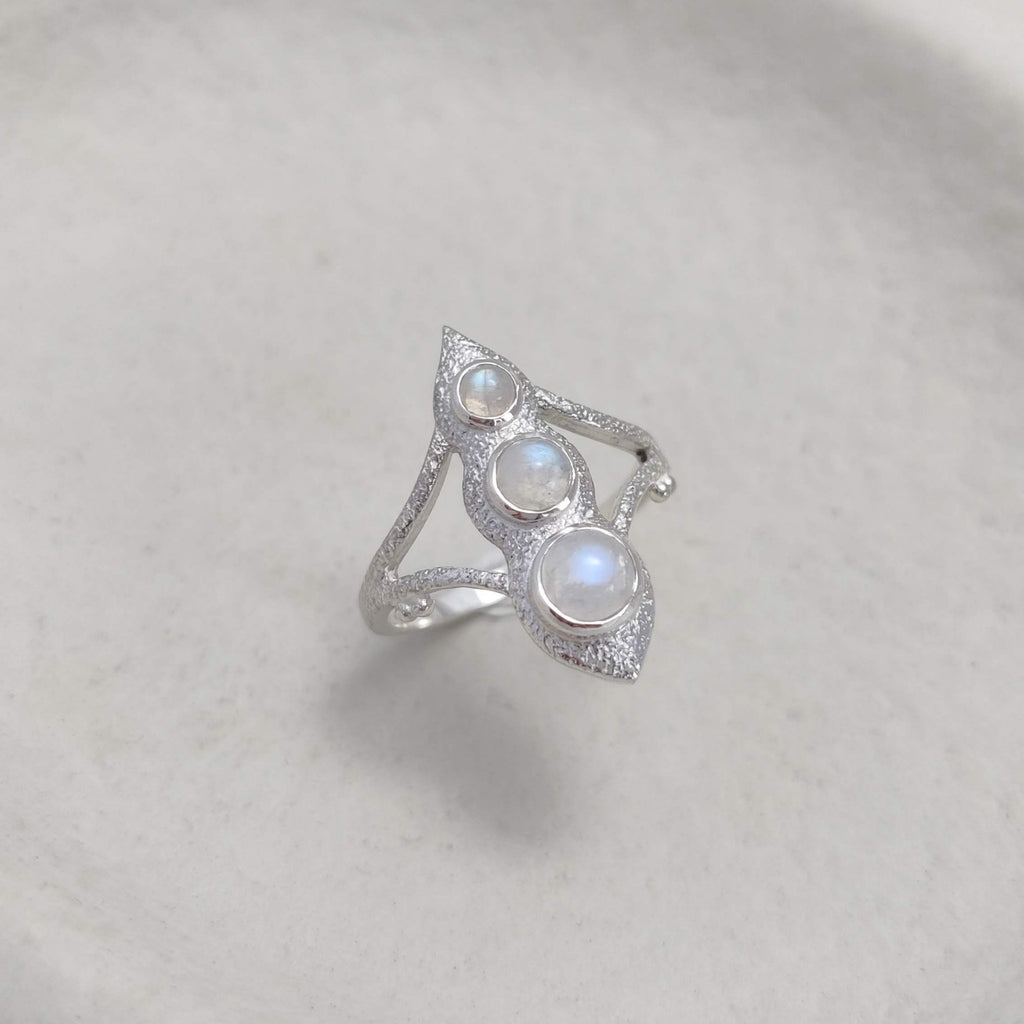 Silver ring with three gemstones on a white ceramic dish.
