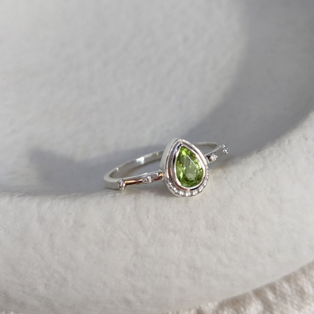 Silver ring with a green gemstone on a textured white surface.