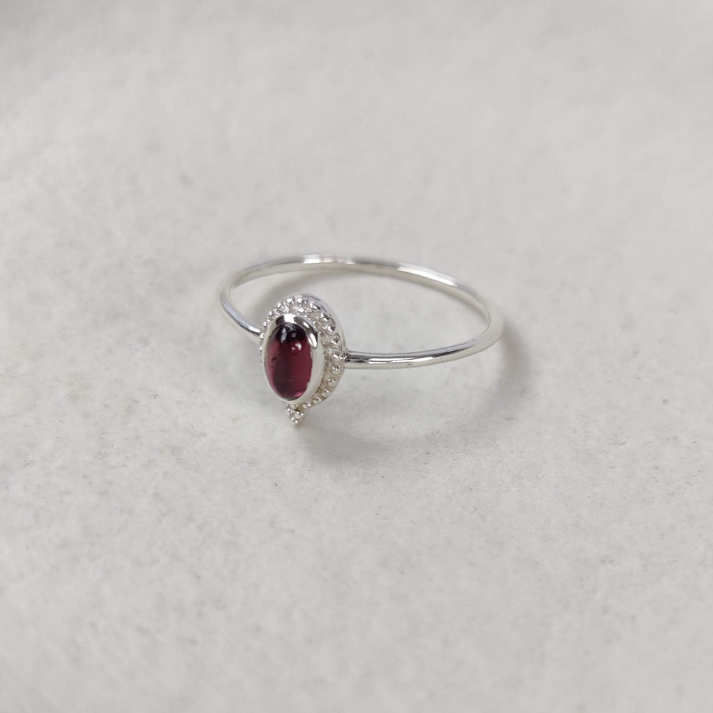 Delicate silver ring with red garnet gemstone on white background