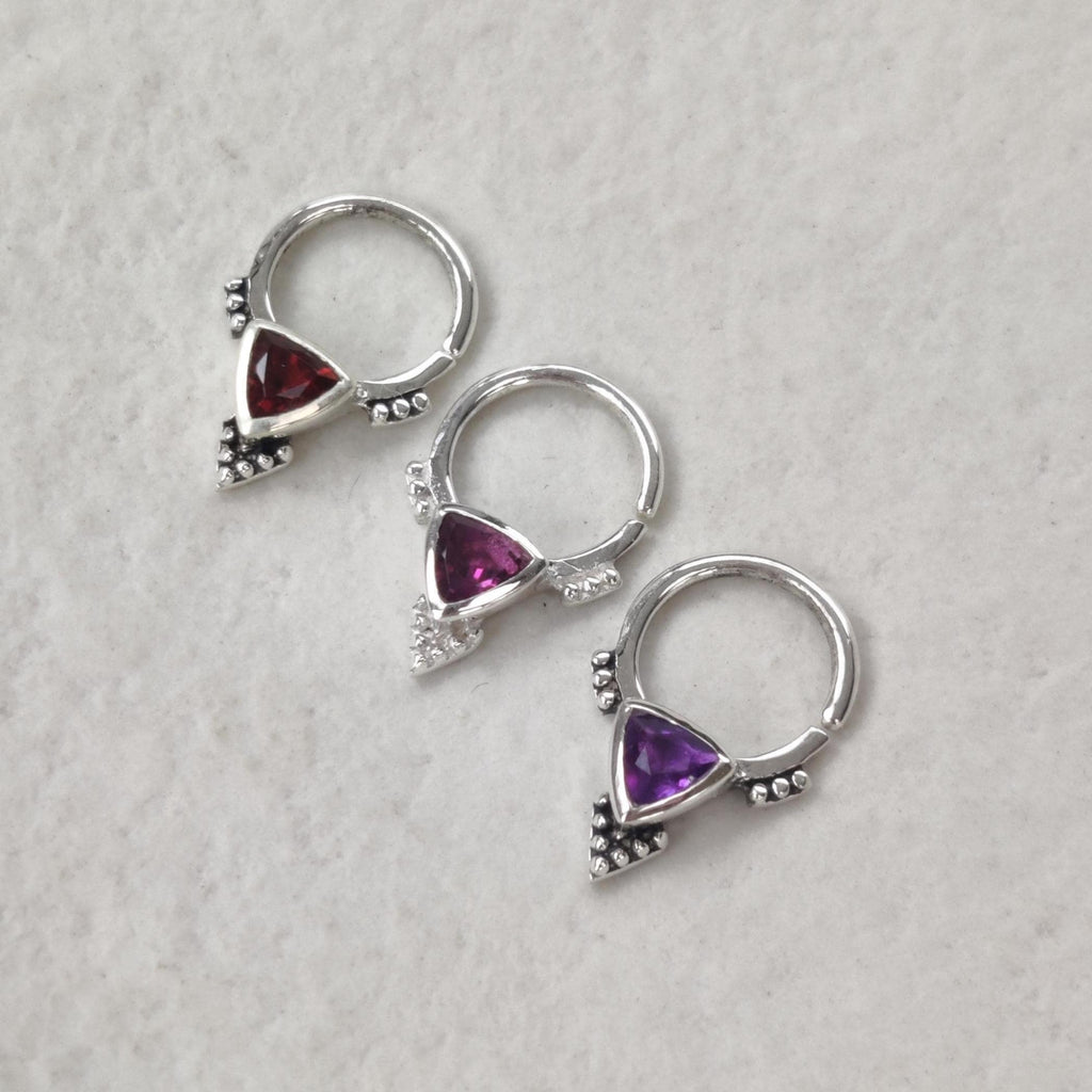Three pieces of silver septum jewelry with triangle shaped gemstones. Garnet, rhodolite garnet and amethyst