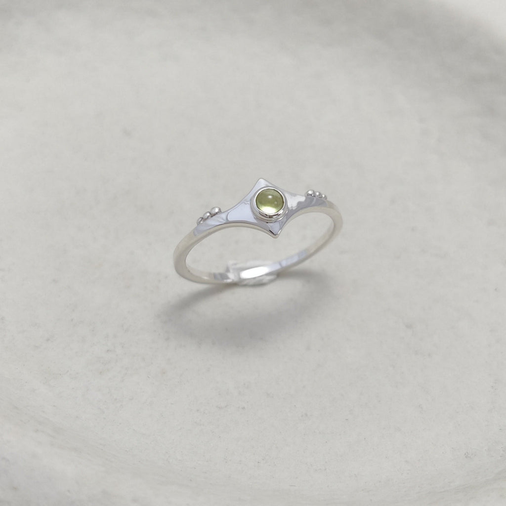 Silver ring with a green gemstone on a white ceramic dish.