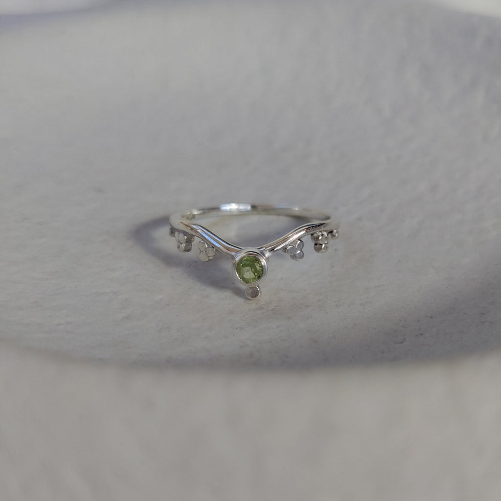 Silver ring with a green gemstone on a textured surface.