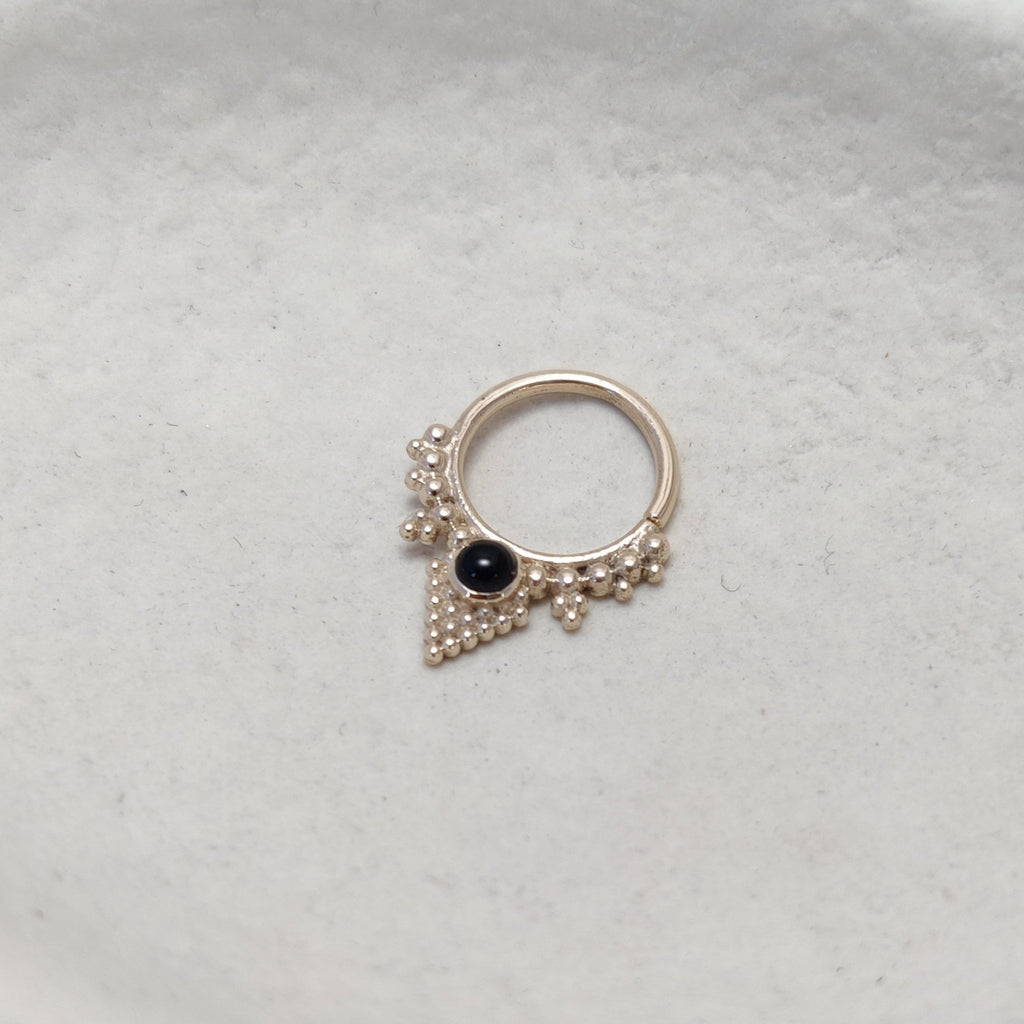 Solid gold septum with black onyx gemstone, displayed on a jewelry plate.