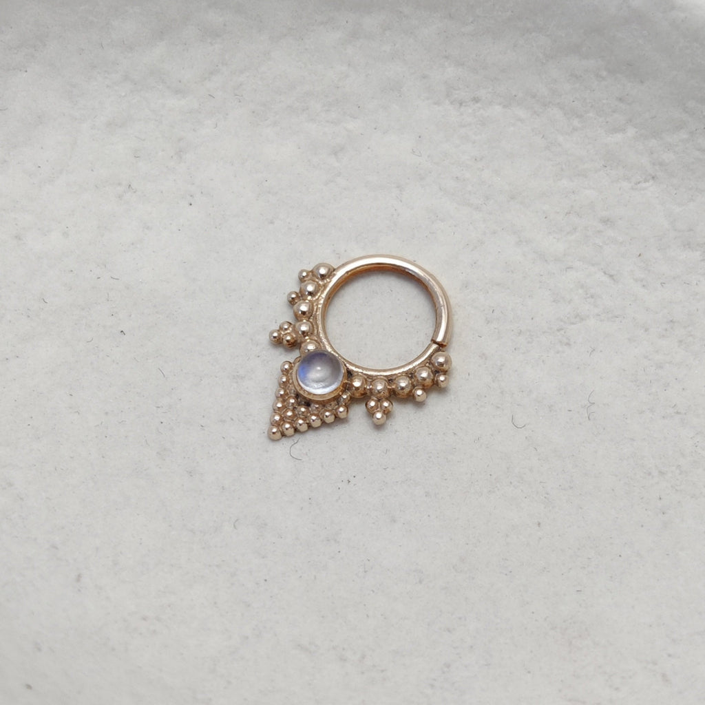 Solid gold septum with moonstone, displayed on a jewelry plate.