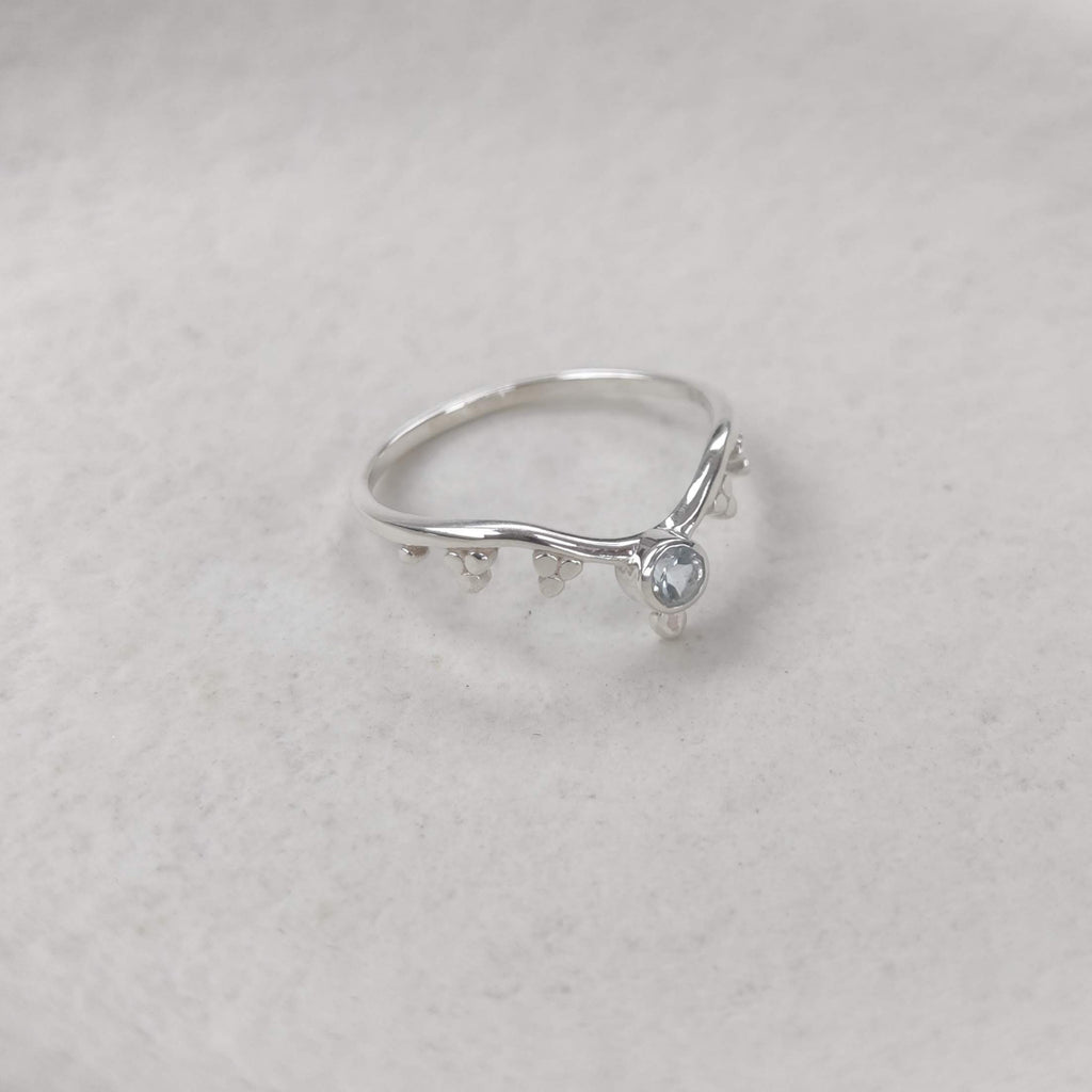 Silver stacking  ring with small blue topaz gemstone on a light background.