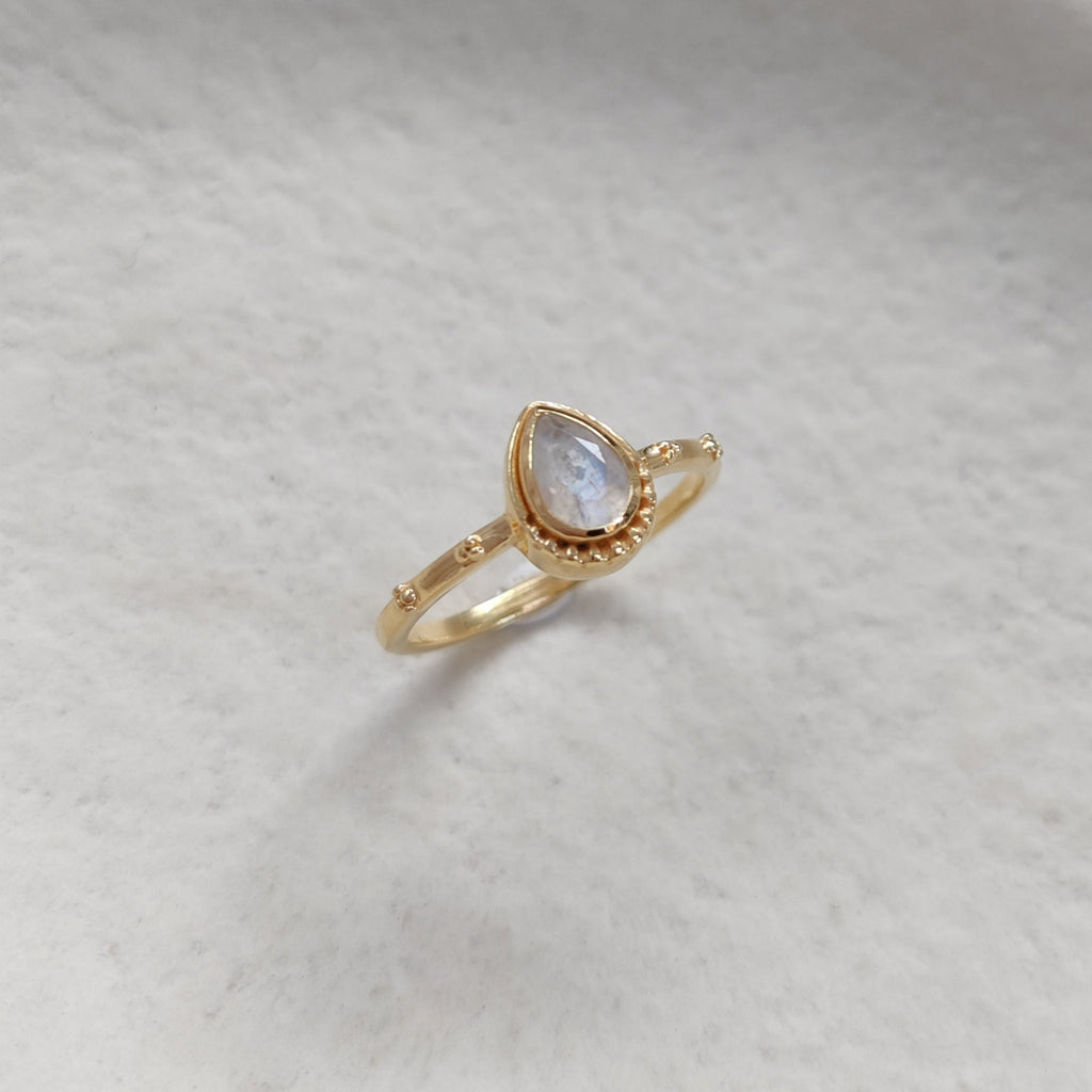 Gold ring with a shimmering moonstone on a white surface.