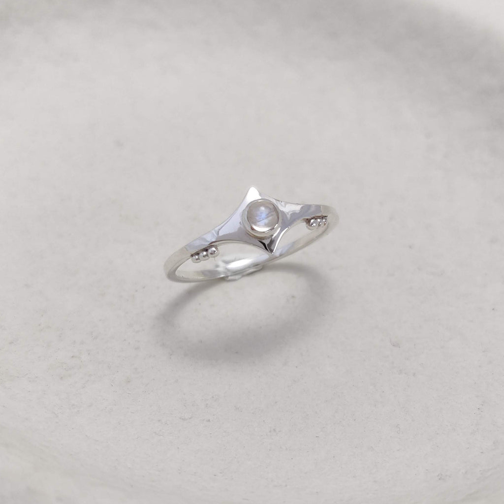 Silver ring with a small moonstone on a textured white surface