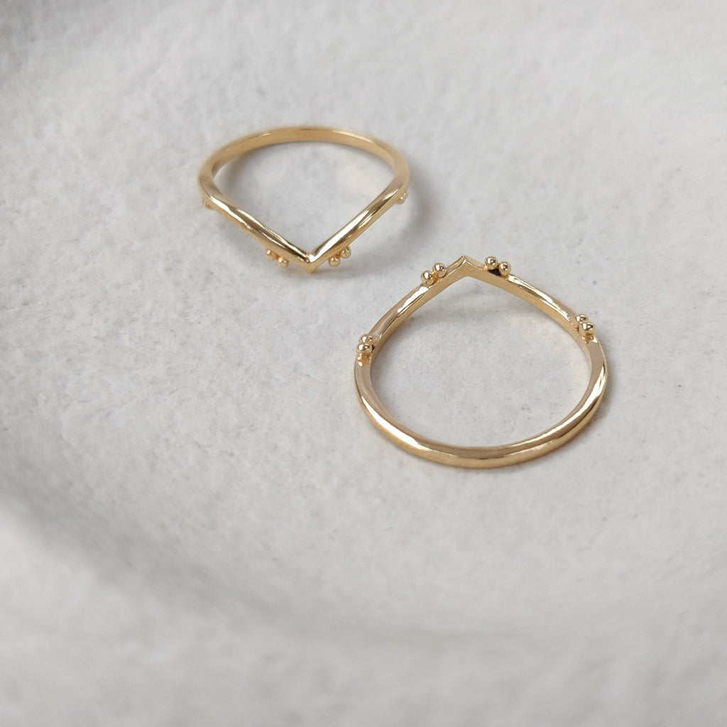 Two v-shaped gold rings on a textured white surface.