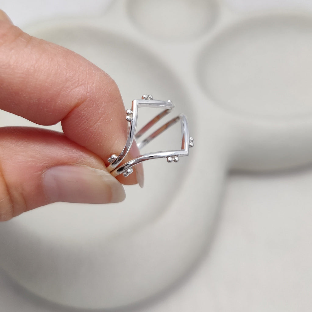 Silver stacking rings held by a hand against a white background.