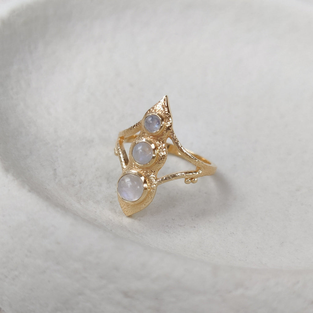 Gold ring with three gemstones on a white ceramic dish.