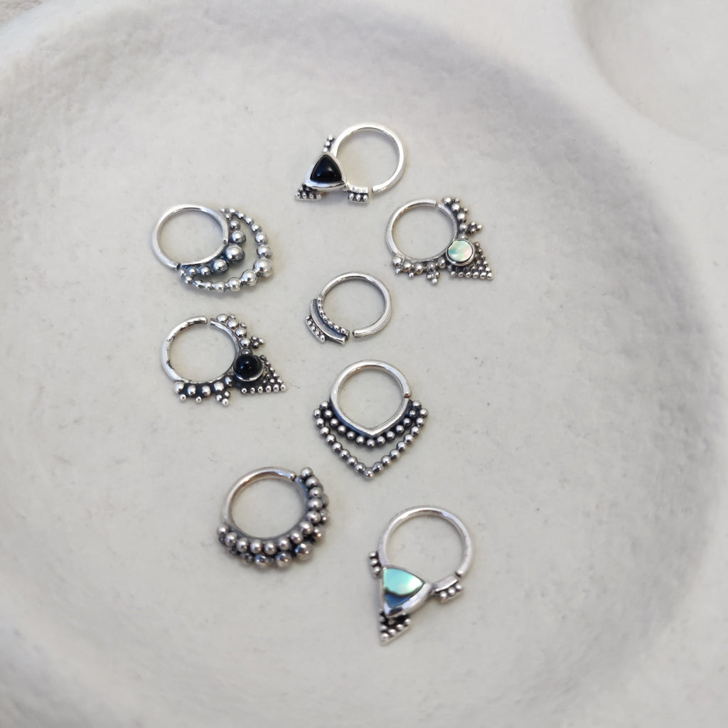 A collection of silver septum jewelry featuring intricate dotted details and gemstones, displayed to showcase their unique designs. Noomaad design.