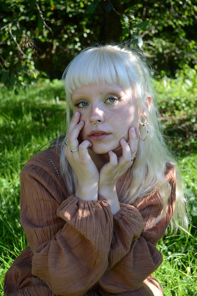 Woman with blonde hair, a septum nose ring and silver rings with black gemstones sitting on grass