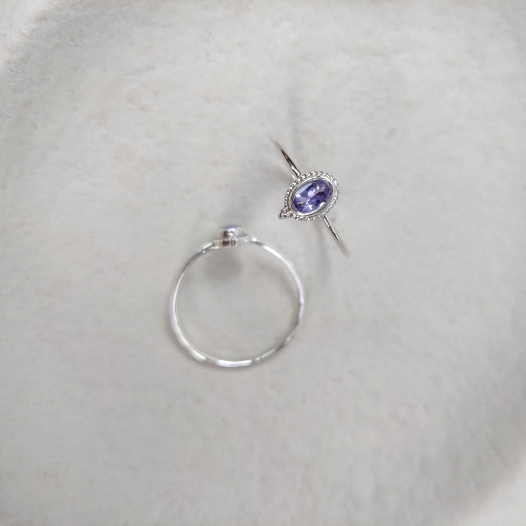 Silver rings with a blue-purple gemstone on a light background, displayed from different angles.