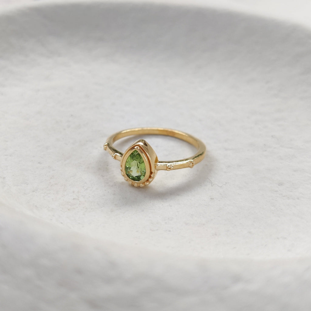 Tear-drop shaped gold ring with a green gemstone on a white surface.