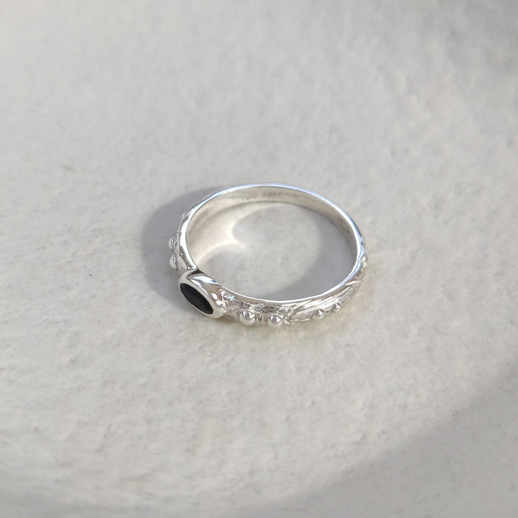 Silver ring with a black gemstone on a textured white surface.